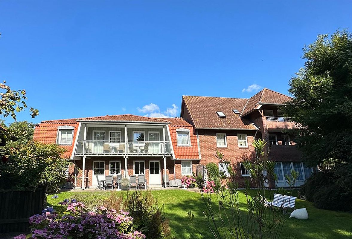 Garten einer Ferienanlage mit einem Ferienhaus und Balkonen im Hintergrund